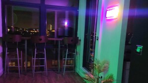 A room with a large window, a small plant, and a bar area with stools. - Bull's Ring 3bed Penthouse City Centre (Birmingham)