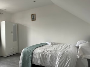 A bedroom with a bed, white walls, a wardrobe, and a framed picture on the wall. - Remarkable 1-bed Studio Apartment in Redbridge (Ilford)