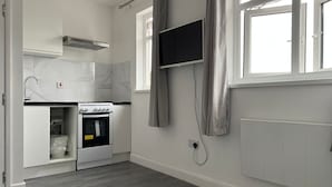 Een moderne keuken met witte kasten, een inbouwoven en een flatscreen tv aan de muur.