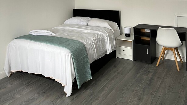 Een moderne slaapkamer met een bed, nachtkastjes, een bureau en een stoel.