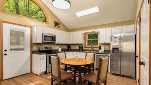 Una cocina con armarios blancos, un refrigerador de acero inoxidable, una mesa de madera redonda y sillas.
