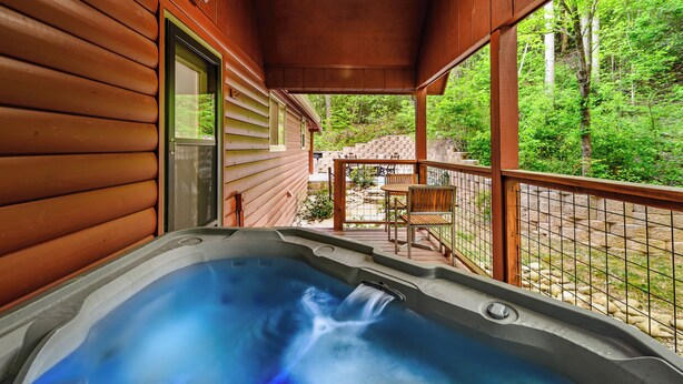 Una cabaña de madera con un jacuzzi en el porche, rodeada de follaje.