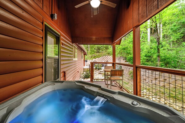 Eine Holzhütte mit Whirlpool auf der Veranda, umgeben von einer Holzterrasse und Blick auf einen Wald.