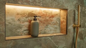 Ein Badezimmer mit Marmorwand, einem gerahmten Spiegel, einer Seifenspende und einem goldfarbenen Duschkopf.