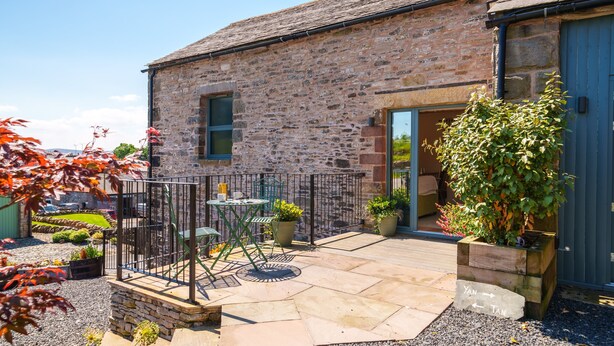 A stone building with a patio area featuring a table and chairs, surrounded by potted plants and a gravel path.
