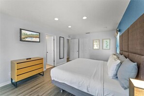 Une chambre à coucher comprenant un lit, une commode, un téléviseur et une porte donnant sur une autre pièce.