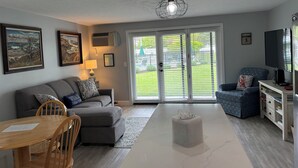 A modern living room with a grey sofa, a wooden dining table, and a TV on a stand. - Ocean Towers 111 Condo (Ogunquit)