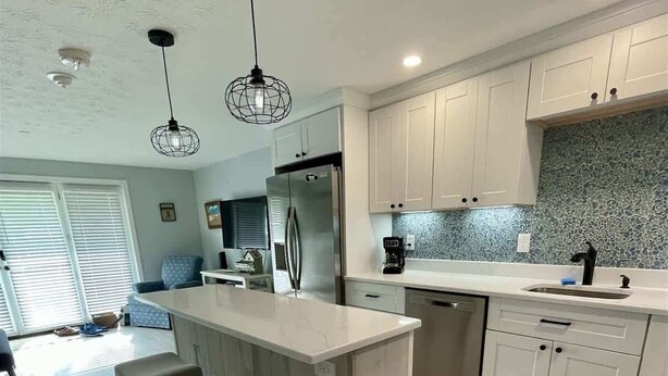 A modern kitchen with a central island, white cabinets, and a backsplash. - Ocean Towers 111 Condo (Ogunquit)