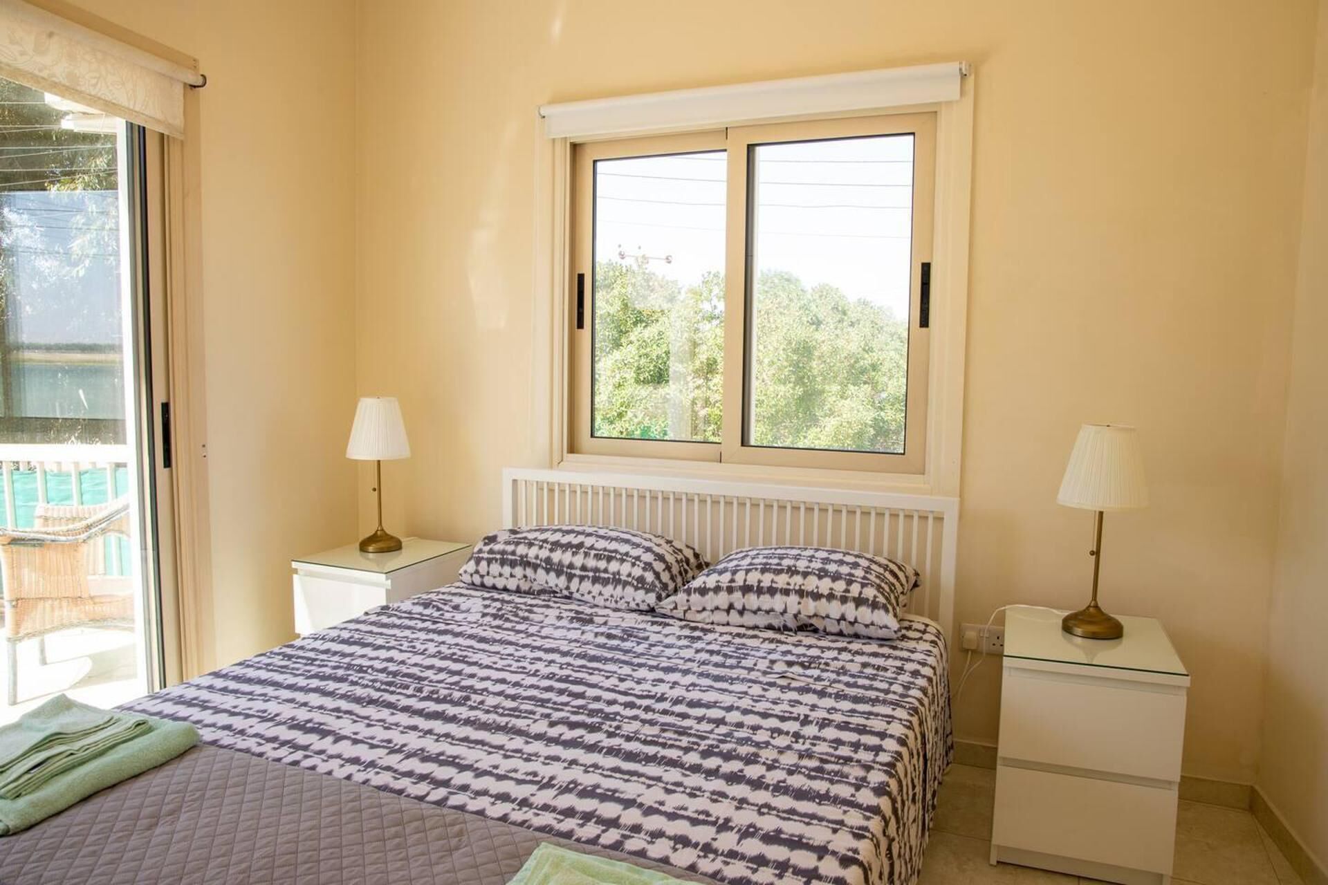 Un dormitorio con una cama, dos mesitas de noche, un ventanal y vistas a zonas verdes.