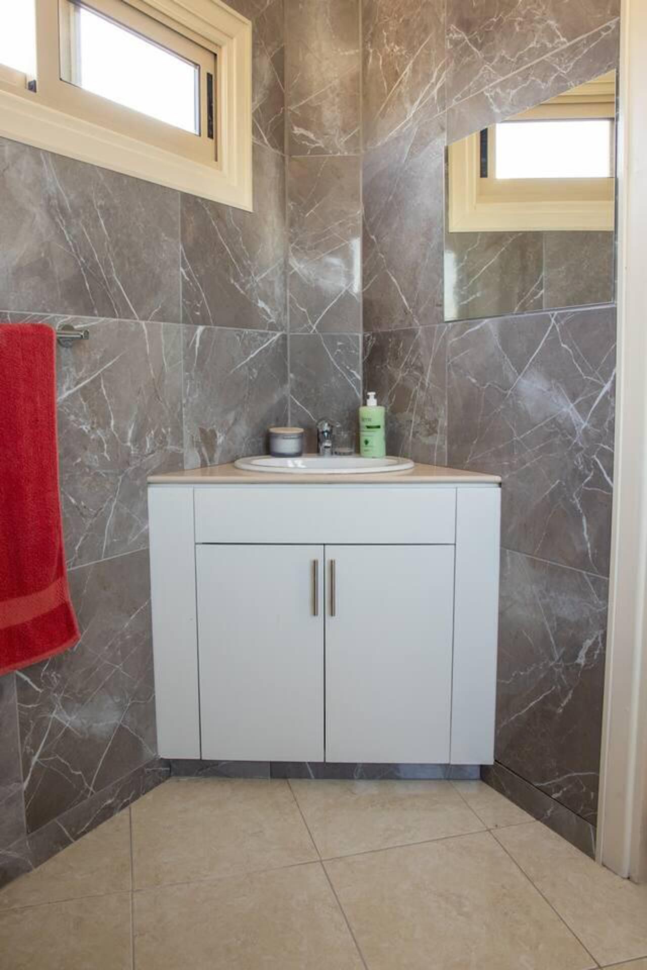 A bathroom with a marble wall, a white sink with a mirror above it, and a red towel hanging on the wall.