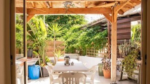 Een open terras met een houten pergola, een witte tafel en stoelen.