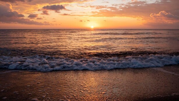 Een zonsondergang boven de oceaan, met golven die op het strand breken.
