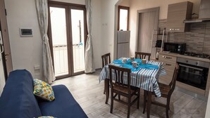 Un salon confortable avec un canapé, une table à manger avec des chaises, un coin cuisine équipé d’une cuisinière et d’un four, et un balcon avec des rideaux.