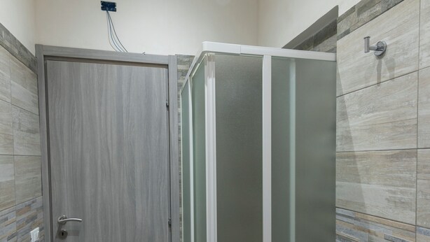 Une salle de bain avec un espace douche fermé, une porte en bois et des murs carrelés.