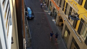 Une rue pavée, bordée de bâtiments des deux côtés, avec une voiture garée et des gens qui se promènent.