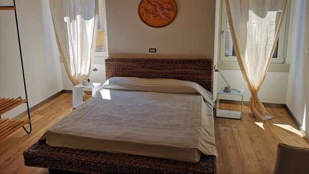 Une chambre à coucher avec un lit, une table de chevet, une lampe, une horloge murale et une fenêtre avec des rideaux.