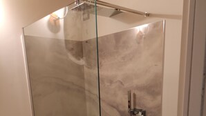 Une douche fermée par des parois en verre, dotée d’un pommeau de douche à main et d’un robinet mural.