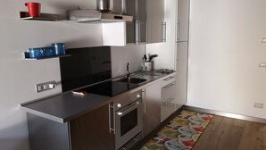 Une cuisine moderne dotée d’appareils électroménagers en acier inoxydable, d’un plan de travail noir et d’un tapis aux motifs colorés représentant des fruits.