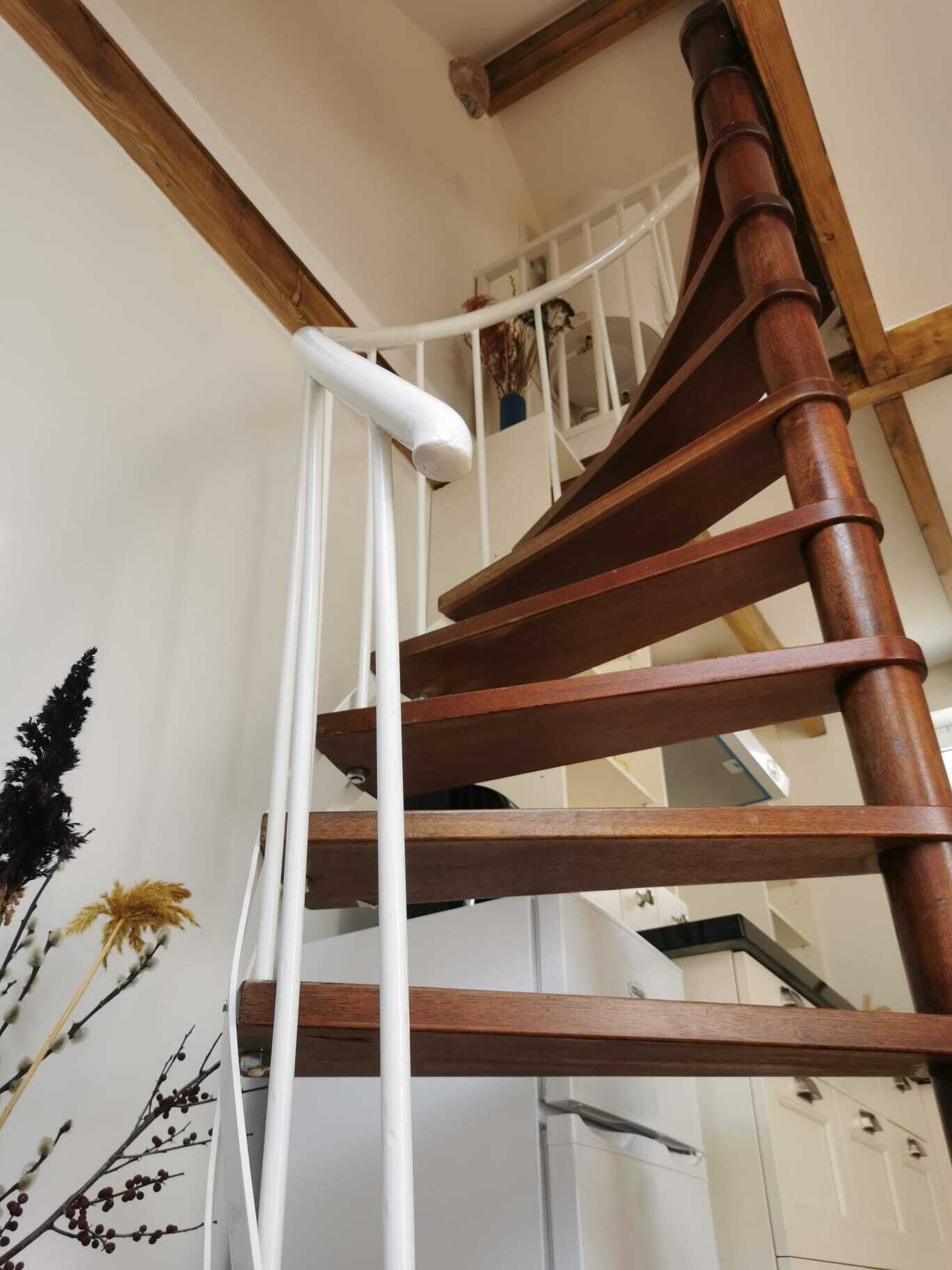 A wooden spiral staircase with white handrails and a white wall with a decorative floral pattern.