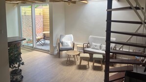 A spacious room with a wooden ceiling, a ceiling fan, a sofa, a chair, a small table, and a staircase.