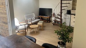 A cozy living room with a sofa, two chairs, a coffee table, a TV, and a staircase.