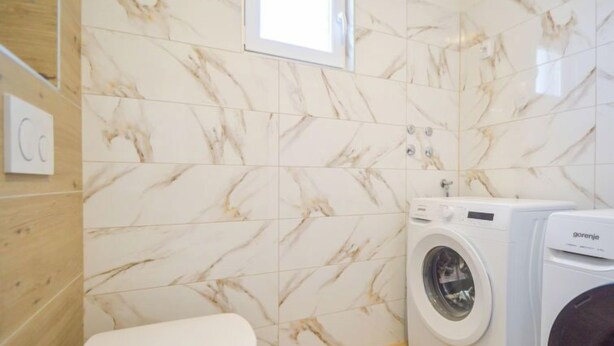 Een kleine badkamer met toilet, wasmachine en een houten vloer.