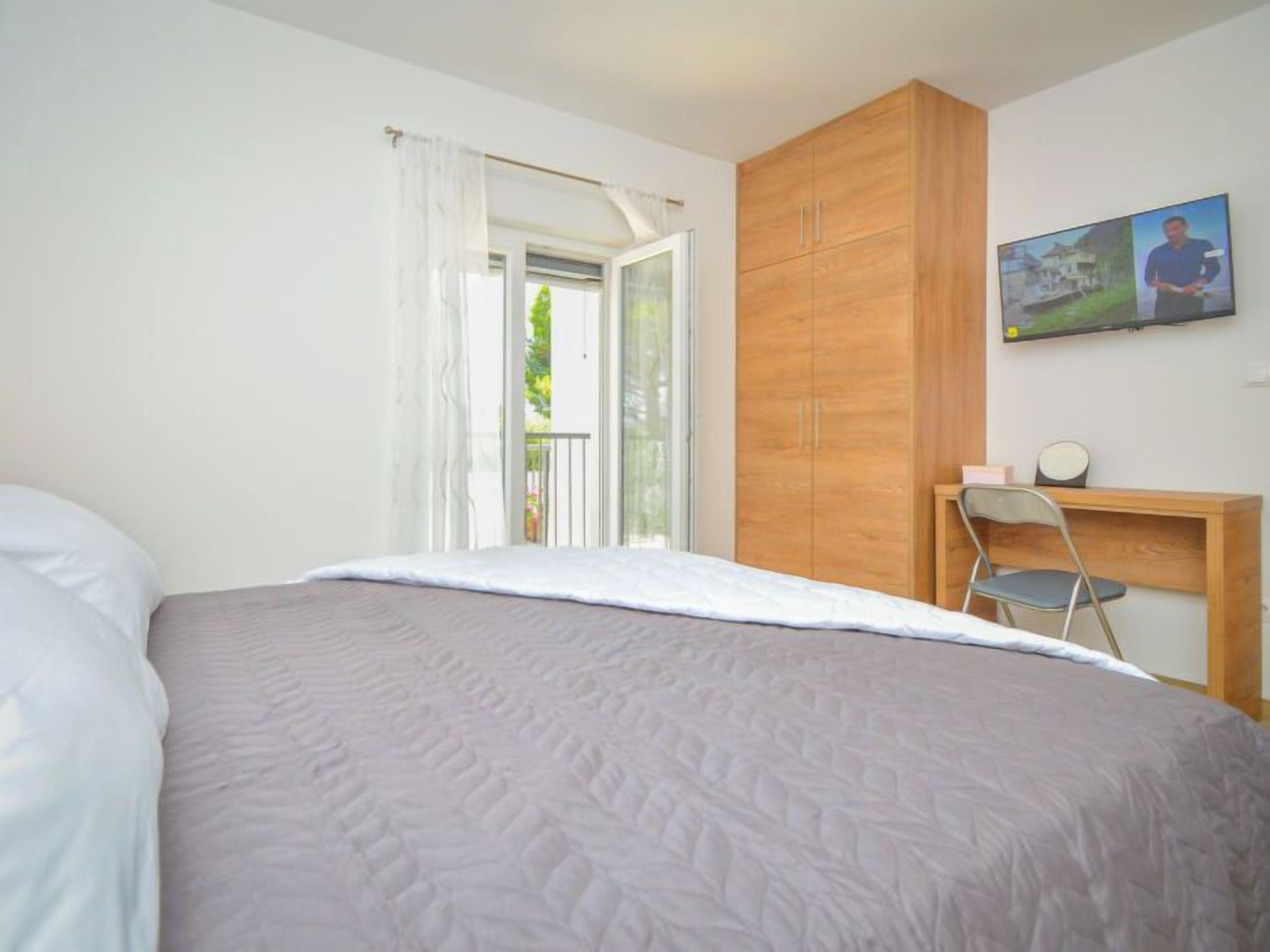 Une chambre à coucher avec un lit, une armoire en bois, un bureau avec une chaise et une fenêtre avec des rideaux.