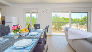 Een eethoek met een tafel voor vier personen, een bank en een balkon met uitzicht op groen.