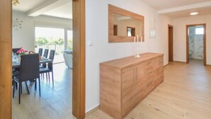 Een ruime kamer met houten vloer, een grote spiegel boven een houten kast, en een eethoek met stoelen en tafel zichtbaar door een open doorgang.