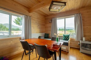 A wooden-paneled room with a dining table, chairs, a bench, and a view of the outdoors. - Furano Log House Farm Resort (Furano)
