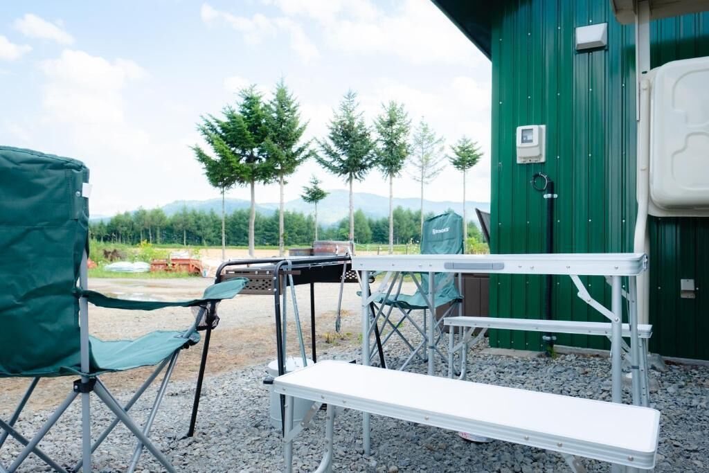 Ein Campingplatz mit einer Sitzbank, einem grünen Klappstuhl und einem Tisch.