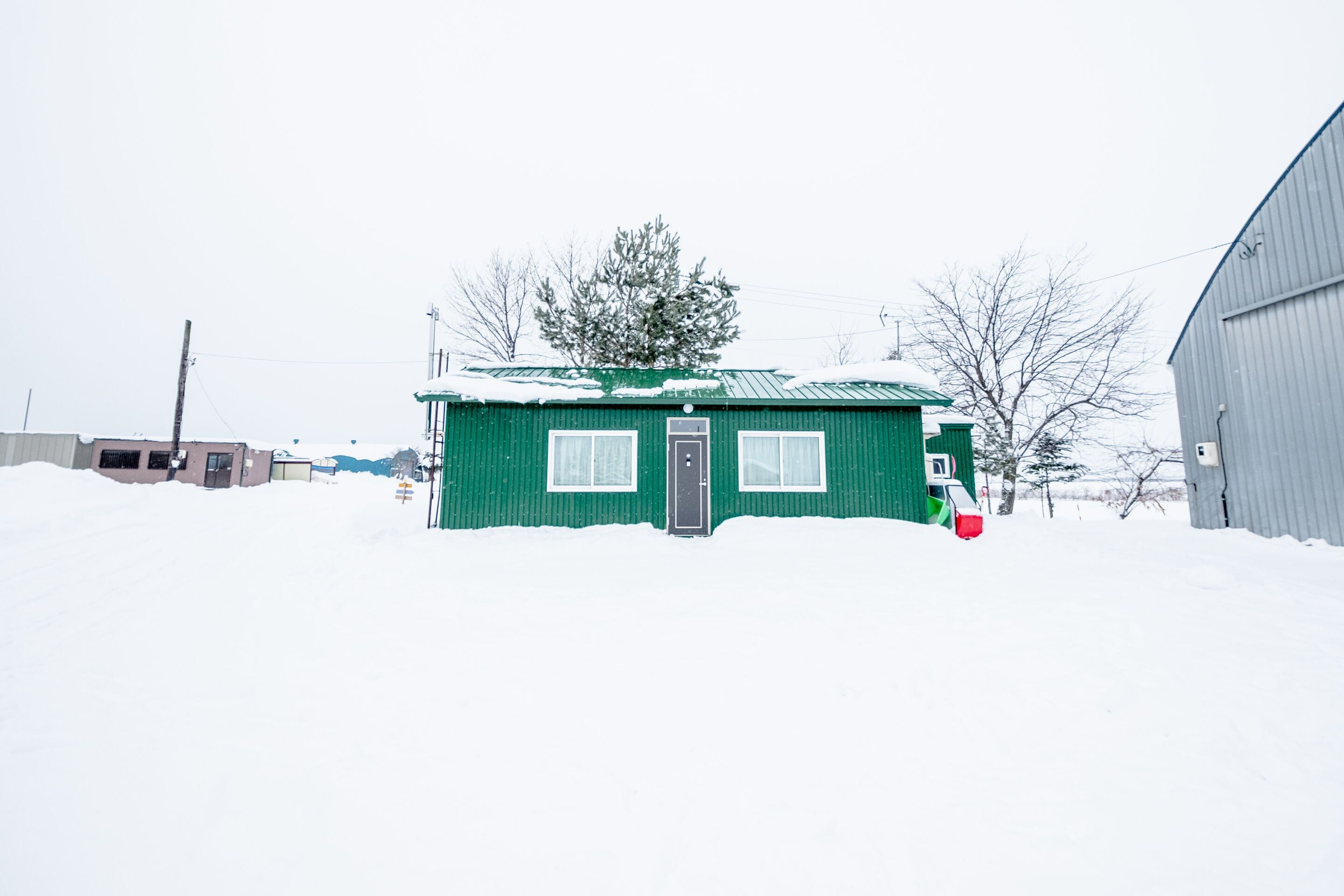 A small green building with a door and windows, surrounded by snow.