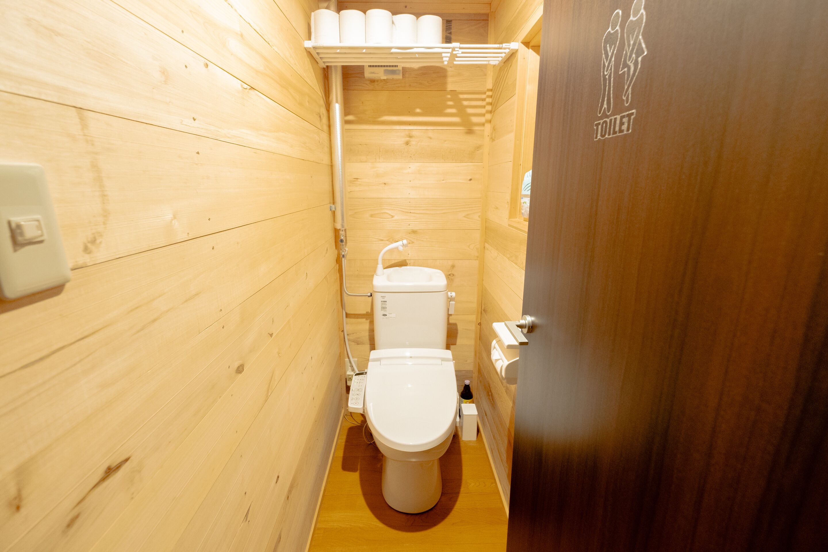 A compact wooden bathroom with a toilet, sink, and toilet paper dispenser.