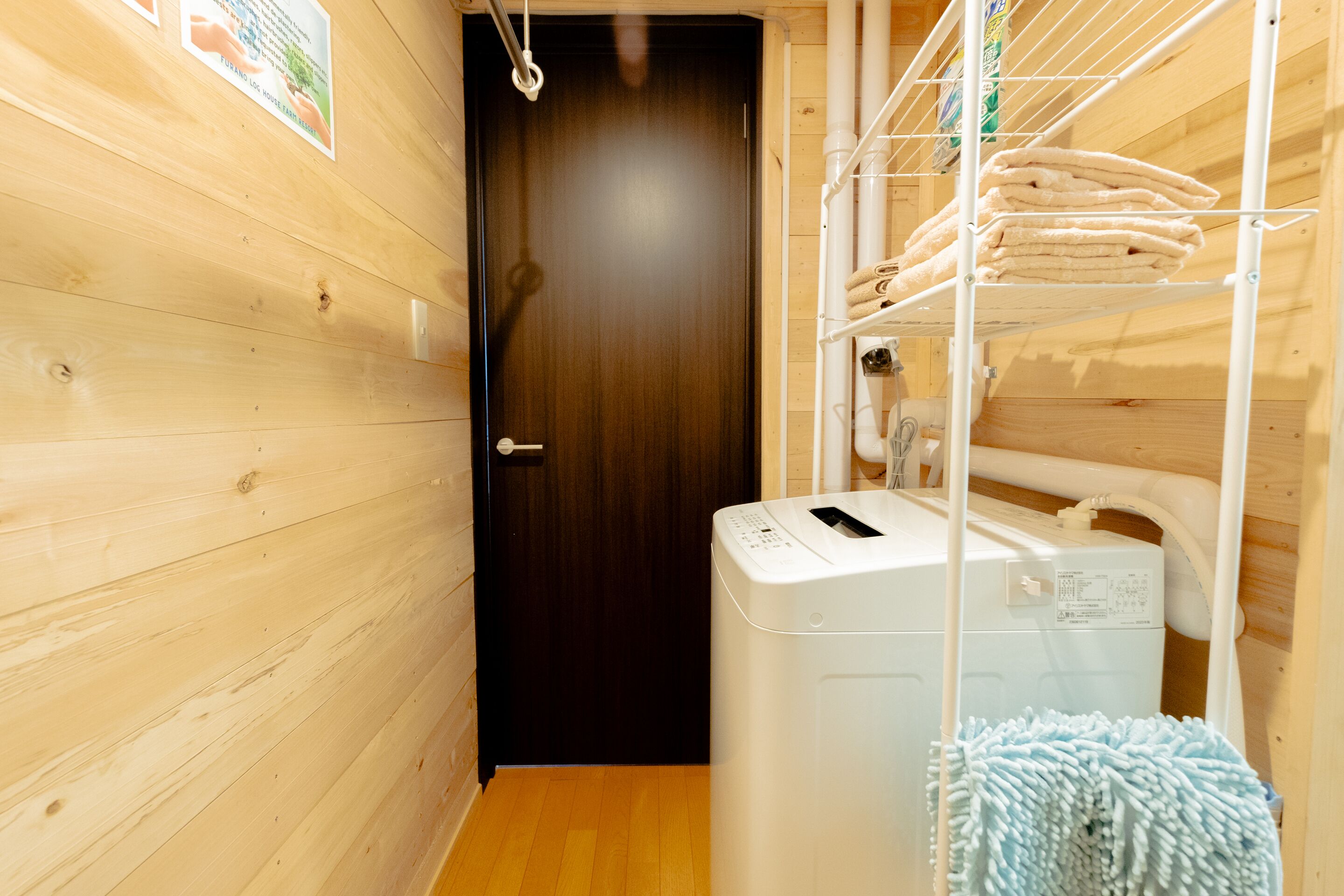 A laundry area with a washing machine, a drying rack, and a wooden door.