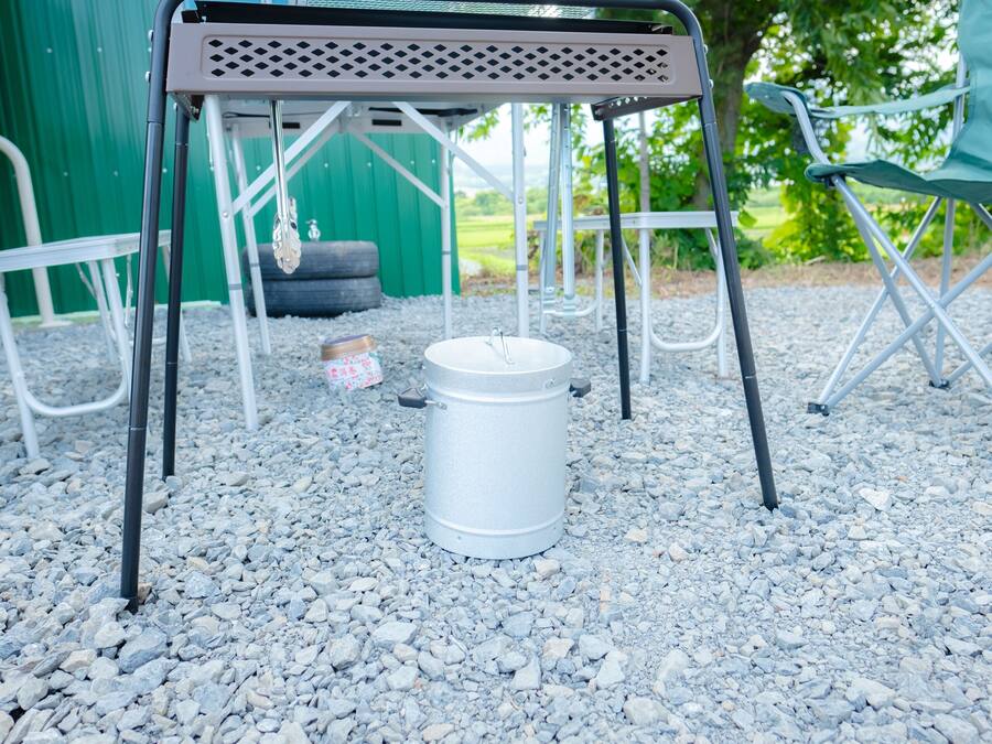 A metal table with a metal frame, a white bucket, and a green chair in a gravel area.