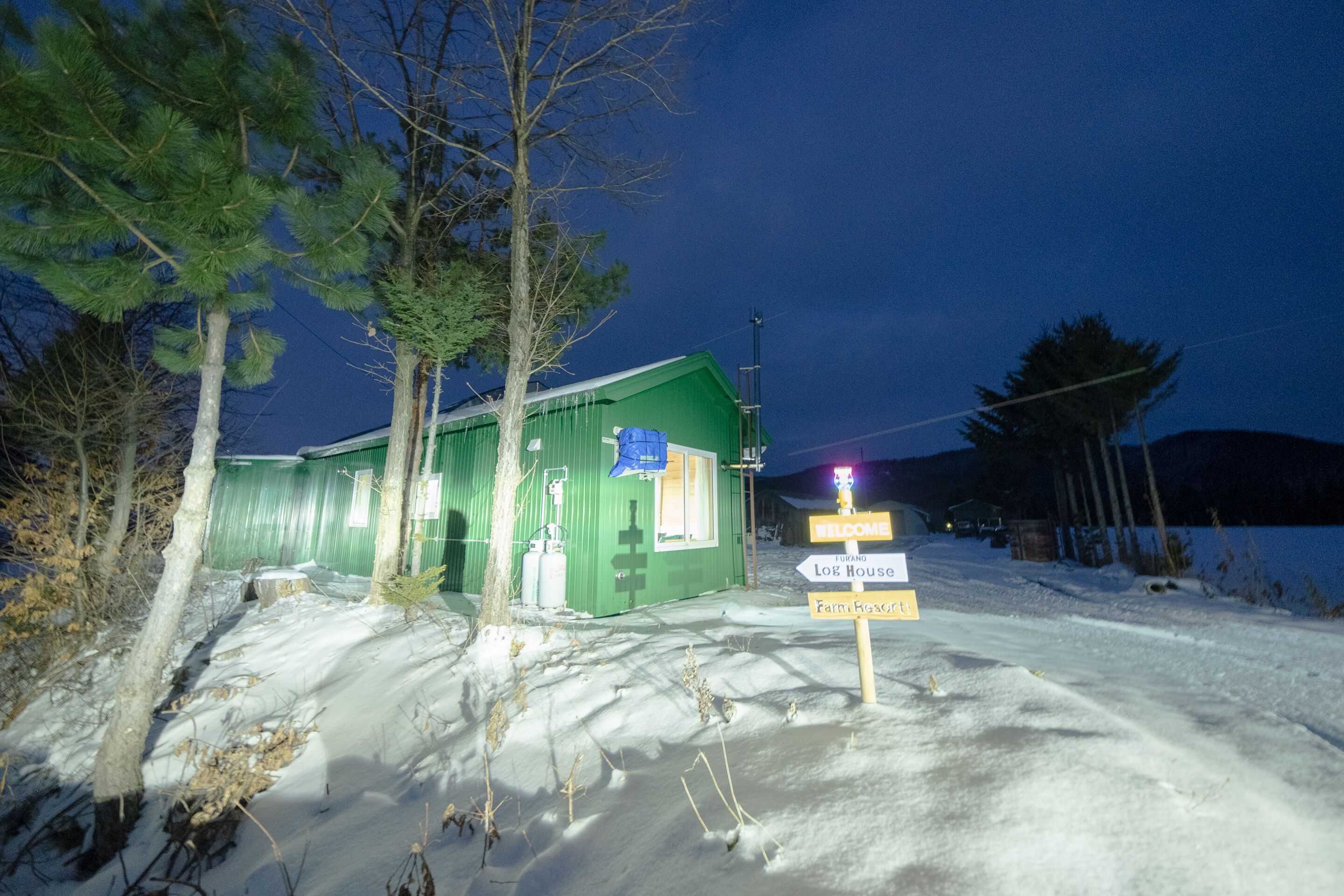 A green building with a sign that reads "Welcome" and "Log House."