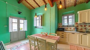 A kitchen with green walls, wooden cabinets, and a dining area with a table and chairs. - Antica Dimora del Platano - F4856 (Nurachi)