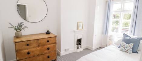 A bedroom with a bed, a dresser, a mirror, a fireplace, and a window with curtains.