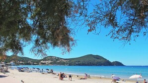 A beach with people sunbathing, umbrellas, and a clear view of the sea and hills in the background. - Les Lavandes by Interhome (Saint Cyr sur mer Les Lecques)