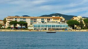 A coastal hotel with multiple floors, a beach in the foreground, and a mountainous backdrop. - Les Dauphins by Interhome (Sainte Maxime)
