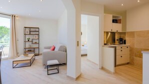 A modern living room with a sofa, a coffee table, and a bookshelf. There is a kitchen area with cabinets and a countertop. - Les Dauphins by Interhome (Sainte Maxime)