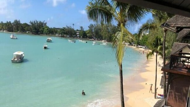 Una playa con agua turquesa cristalina, algunas embarcaciones y una persona caminando por la orilla.
