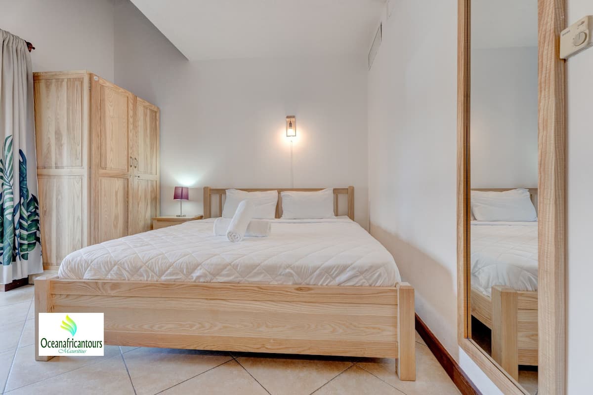 Une chambre à coucher avec un lit en bois, une table de chevet avec une lampe, une armoire et un miroir.