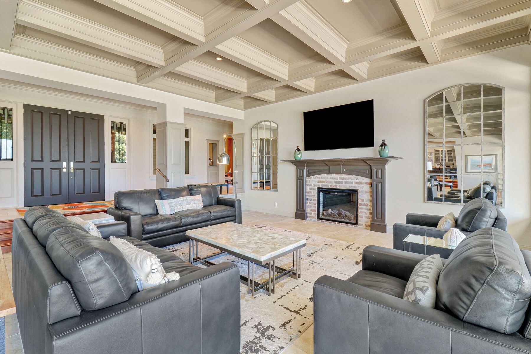 A spacious living room with a fireplace, leather sofas, a flat-screen TV, and a large mirror.