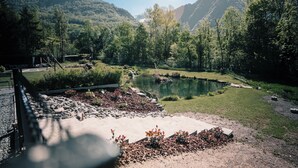Un espace extérieur paisible avec un étang, entouré d’une végétation luxuriante et dominé par des collines en arrière-plan.