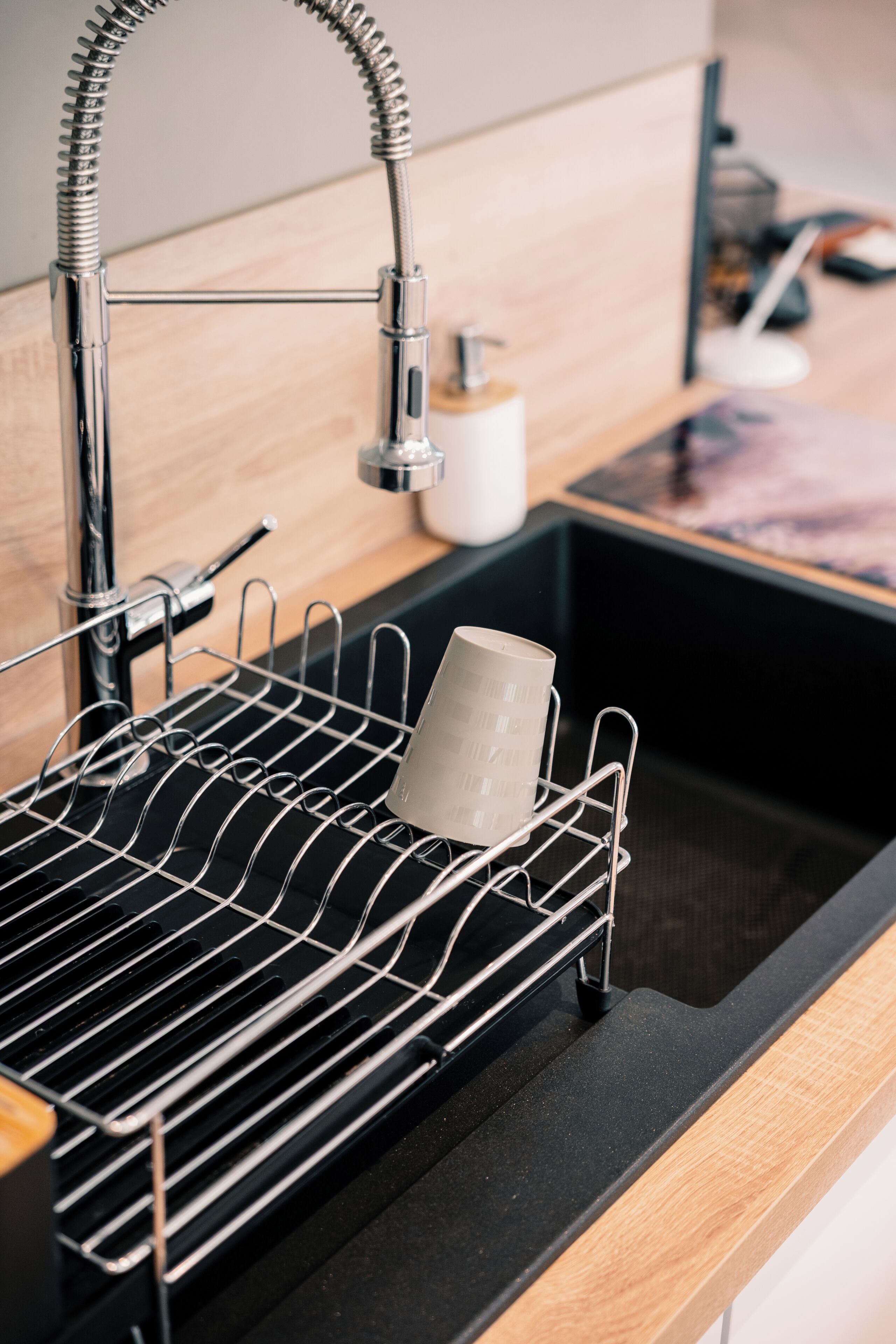 A kitchen sink with a metal drying rack and a white mug.
