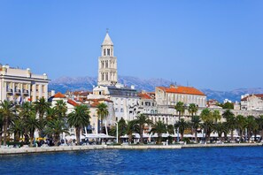 A coastal cityscape with a prominent tower, historic buildings, and a waterfront promenade with palm trees. - Spacious apt few min Walk to old Town and Beach (Split)
