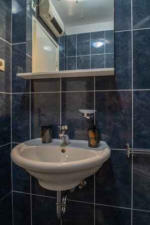 A bathroom with a white sink, dark blue tiles, a mirror, and a towel rack. - Spacious apt few min Walk to old Town and Beach (Split)