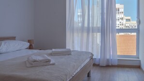 Hotellihuone, jossa on suuri sänky, yöpöytä ja ikkuna, jossa on ohuet verhot.