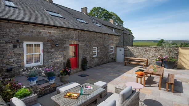 A stone building with a red door, outdoor seating area with wicker furniture, and potted plants. - Fell End - Sleeping 8+5 guests in 4 bedrooms (Brampton)